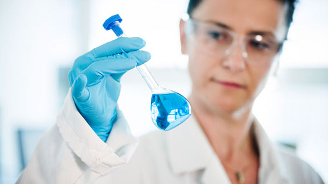 an employee holds a test tube with blue liquid